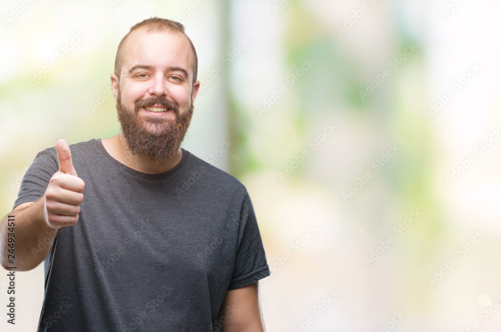 Young caucasian hipster man over isolated background doing happy thumbs up gesture with hand. Approving expression looking at the camera with showing success. Young caucasian hipster man over isolated background doing happy thumbs up gesture with hand. Approving expression looking at the camera with showing success.