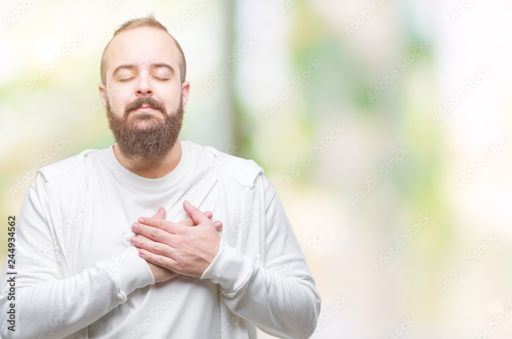 Young caucasian hipster man wearing sport clothes over isolated background smiling with hands on chest with closed eyes and grateful gesture on face. Health concept. Young caucasian hipster man wearing sport clothes over isolated background smiling with hands on chest with closed eyes and grateful gesture on face. Health concept.