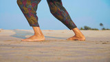 Feet of active senior woman practicing tai chi gymnastic on sandy beach.