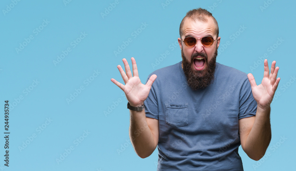 Naklejka premium Young caucasian hipster man wearing sunglasses over isolated background celebrating crazy and amazed for success with arms raised and open eyes screaming excited. Winner concept