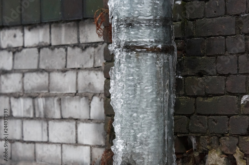 Drainpipe covered with ice and icicles/copy space, dangerous situation, danger for passers, сold winter, poor thermal insulation, ice stalactite, formation of icicles, frost and winter weather concept