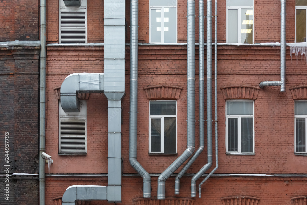 Metal ventilation pipes run along the facade of a brick house outdoor