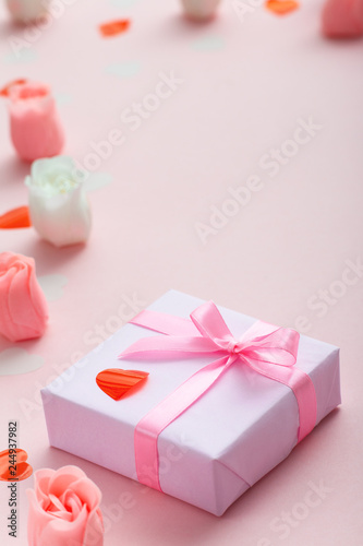 background of gifts with confetti hearts and roses, boxes wrapped in decorative paper on pastel colored pink background, holiday concept and love