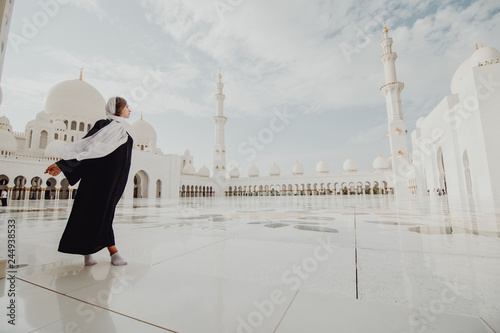 Traveling by United Arabic Emirates. Young woman in traditional abaya standing in the Sheikh Zayed Grand Mosque, famous Abu Dhabi sightseeing. photo