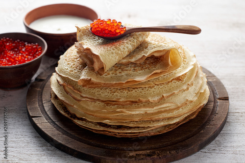 Stack of russian thin pancakes blini with red caviar and fresh sour cream