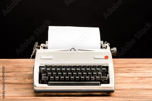 vintage typewriter with paper on wooden table isolated on black