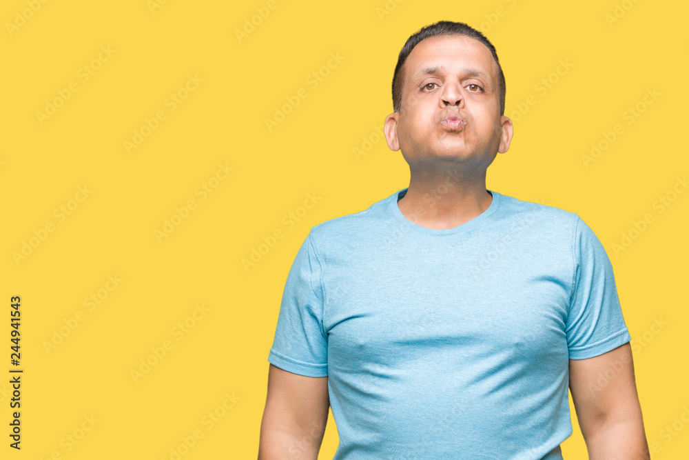 Middle age arab man wearing blue t-shirt over isolated background puffing cheeks with funny face. Mouth inflated with air, crazy expression.