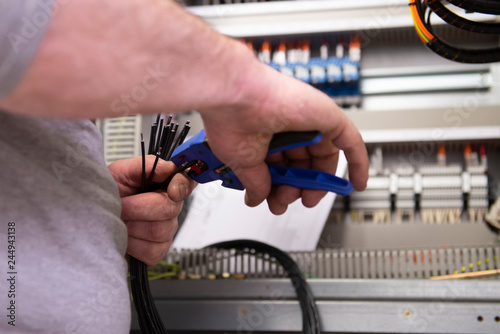 mains d'un électricien qui dénude des fils électriques sur une installation industrielle