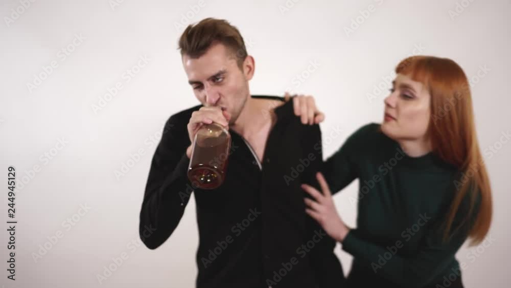 Emotional caring loving wife leaning to her depressed alcoholic husband and feeling desperate while trying to take a bottle of alcohol from him. Emotional caring loving wife leaning to her depressed alcoholic husband and feeling desperate while trying to take a bottle of alcohol from him.