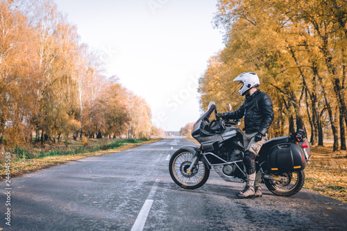 Biker man in leather jacket and black tourist motorcycle with side bags. wallpaper concept, enduro advetnture, space for text, autmn season