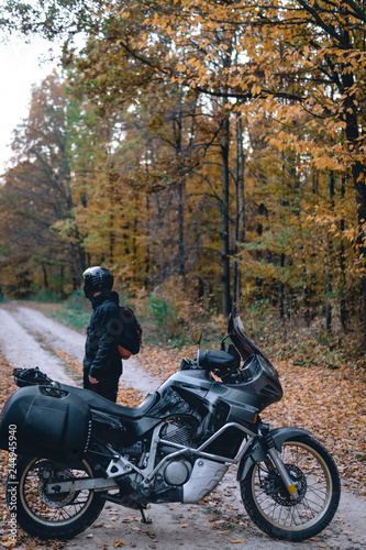 Biker man in leather jacket and black tourist motorcycle with side bags. wallpaper concept, enduro advetnture, space for text, autmn season, vertical photo