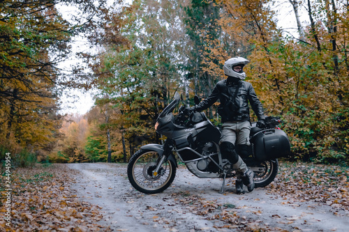 Biker man in leather jacket and black tourist motorcycle with side bags. wallpaper concept, enduro advetnture, space for text, autmn season
