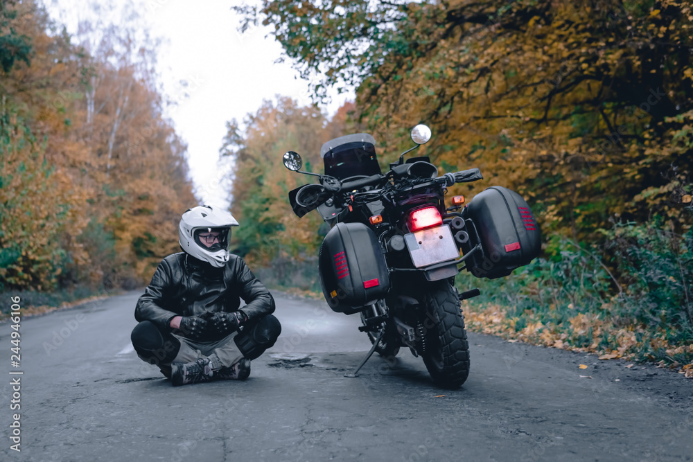 Biker man in leather jacket and black tourist motorcycle with side bags. wallpaper concept, enduro advetnture, space for text, autmn season, problems on the road accident Biker man in leather jacket and black tourist motorcycle with side bags. wallpaper concept, enduro advetnture, space for text, autmn season, problems on the road accident