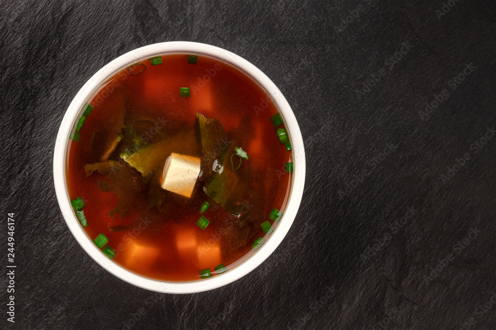 A photo of a bowl of miso shiru soup with tofu, scallions, and wakame seaweed, shot from the top on a black background with copy space A photo of a bowl of miso shiru soup with tofu, scallions, and wakame seaweed, shot from the top on a black background with copy space
