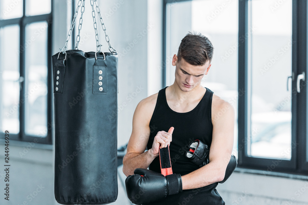 handsome young sportsman wearing boxing glove in gym