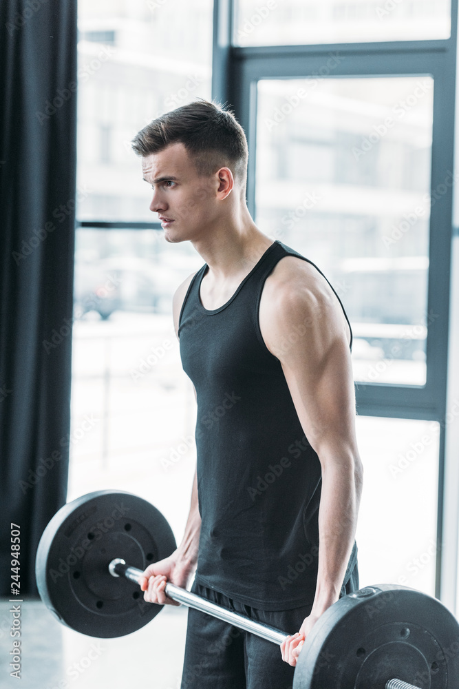 concentrated young sportsman lifting barbell and looking away in gym concentrated young sportsman lifting barbell and looking away in gym