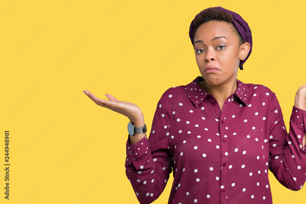 Beautiful young african american woman wearing head scarf over isolated background clueless and confused expression with arms and hands raised. Doubt concept.