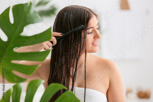 Young woman combing beautiful long hair in bathroom photo