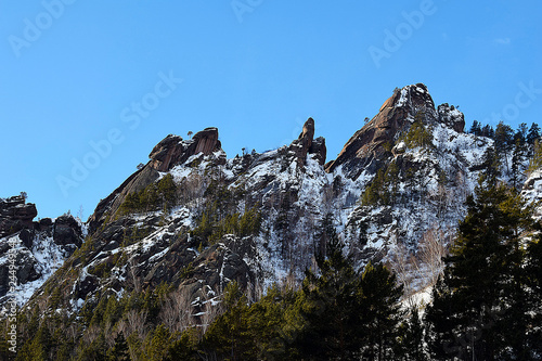 Panoramic mountain view. The peak of a high cliff. Snow on top of the mountain. Clear blue sky.