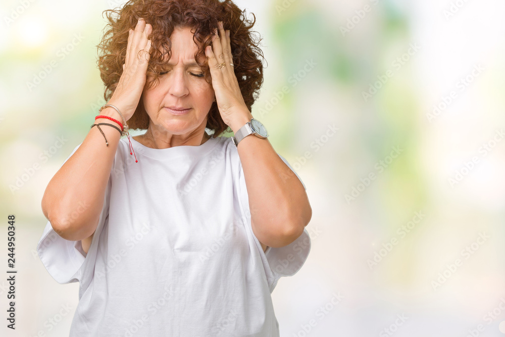 Beautiful middle ager senior woman wearing white t-shirt over isolated background with hand on head for pain in head because stress. Suffering migraine.