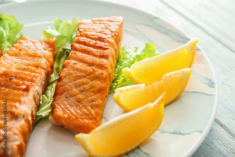 Pieces of tasty grilled salmon with lettuce salad and lemon on plate, closeup Pieces of tasty grilled salmon with lettuce salad and lemon on plate, closeup
