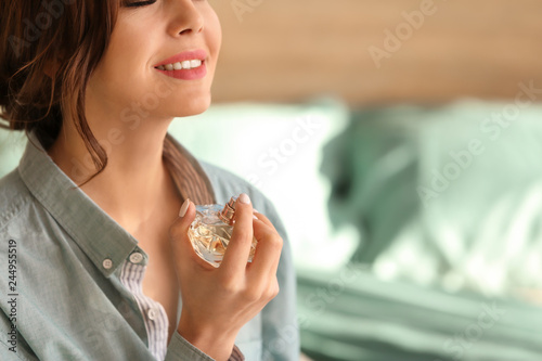 Beautiful young woman with bottle of perfume in bedroom