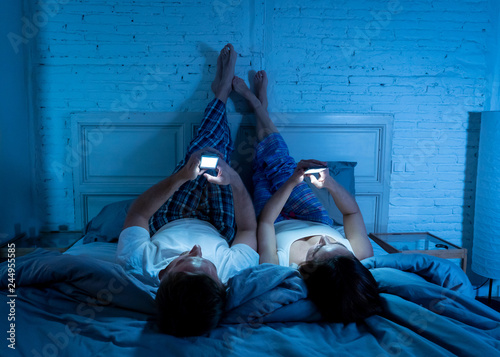 Fotografie Couple on mobile phones in bed late at night enjoying social network, games and