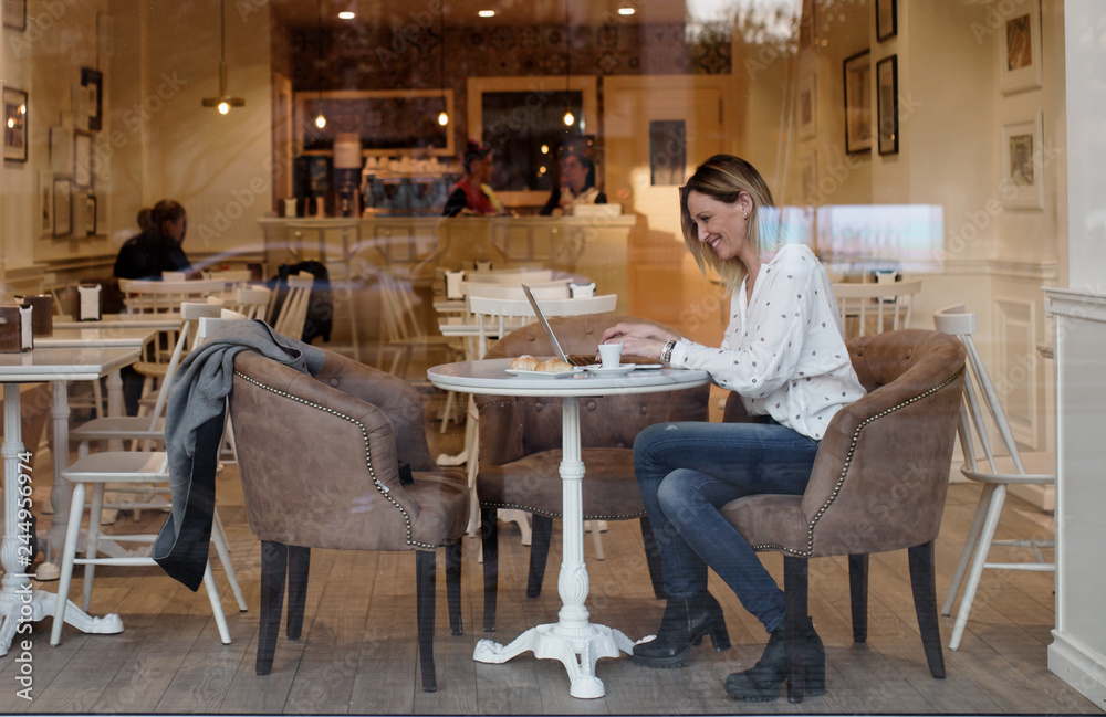 Outside view through a glass of young business woman taking a coffee and working in her laptop Outside view through a glass of young business woman taking a coffee and working in her laptop