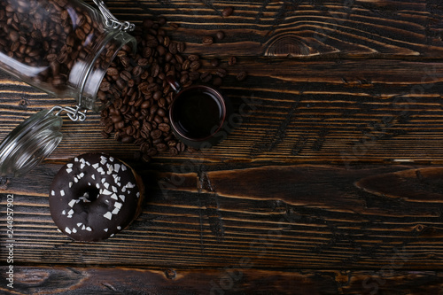 Donut with black icing and chocolate powder and an authentic cup of strong coffee. A can of coffee beans and poured grains. photo