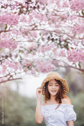 Beautiful asian young woman wearing hat outdoors in a forest. Pretty asian girl model over blur flower background in garden.