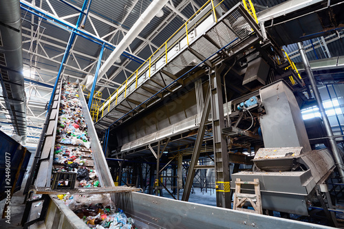 Wide angle view at recycling plant conveyor belt transports garbage inside drum filter or rotating cylindrical sieve with trommel
