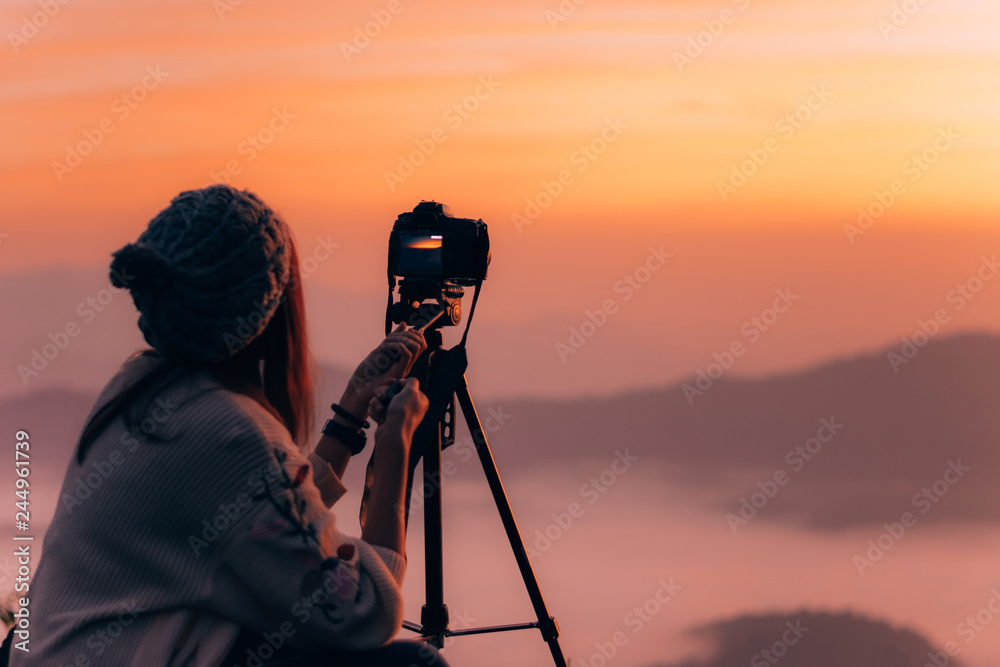 Young woman photographer taking picture of landscape when sunrise  at mountain peak.Travel and hobbies concept