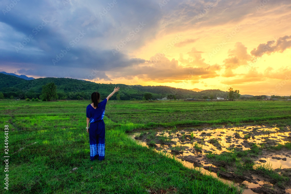 Young woman is looking green field with mountains at sunset.