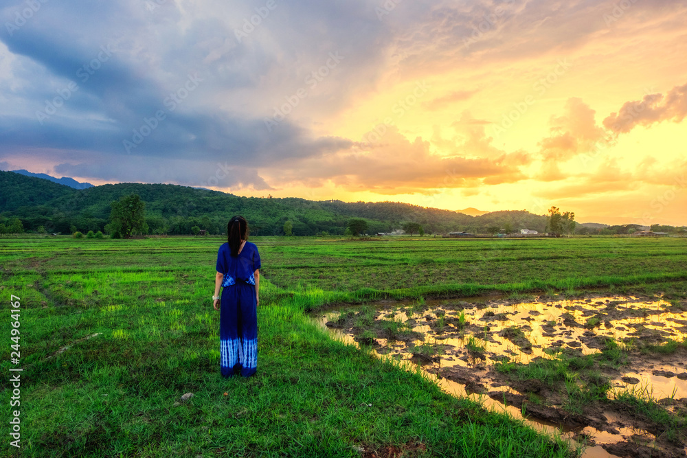 Young woman is looking green field with mountains at sunset.