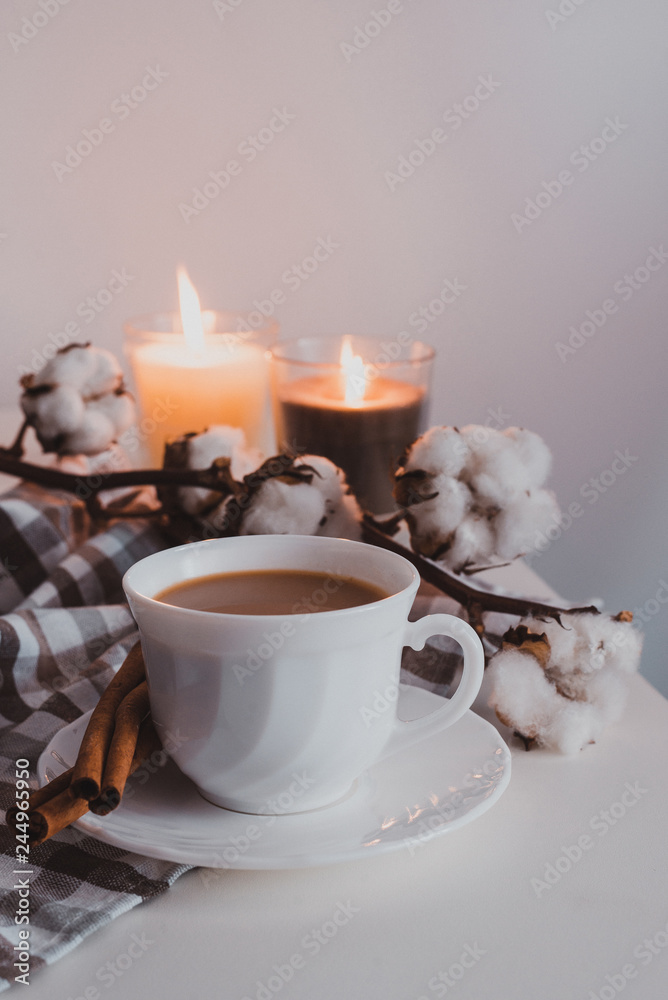 The perfect morning begins with coffee and home comfort. The photo shows a white cup with a saucer, cotton flowers, napkin, cinnamon and candles. The perfect morning begins with coffee and home comfort. The photo shows a white cup with a saucer, cotton flowers, napkin, cinnamon and candles.