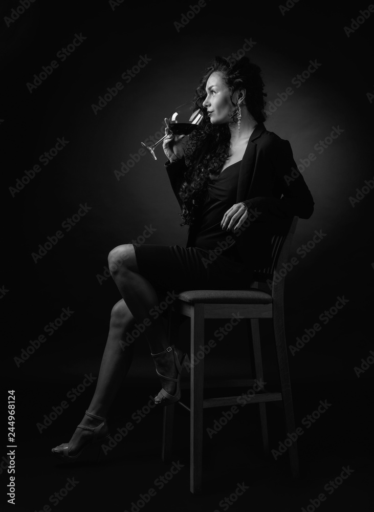 Obraz premium Portrait of attractive brunette with glass of wine on a black bacground.