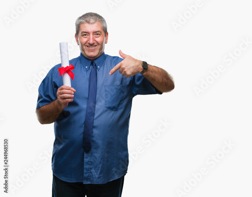 Handsome senior man holding degree over isolated background with surprise face pointing finger to himself