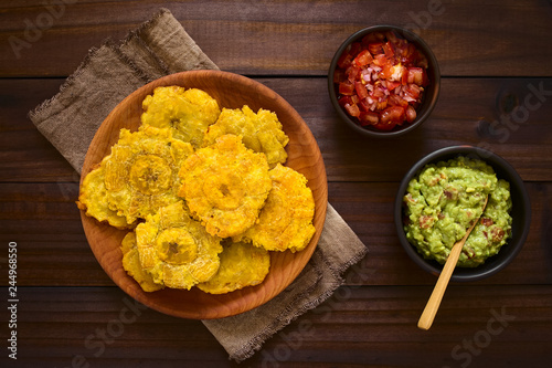 Patacon or toston, fried and flattened pieces of green plantains, traditional snack or accompaniment in the Caribbean, guacamole and tomato onion salad on the side