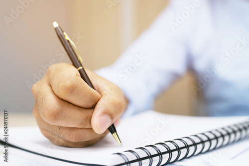 close up hand young man are sitting using pen writing Record Lecture note pad into the book on the table wood.