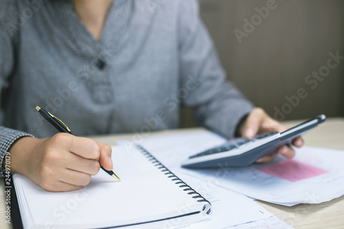 Close up young woman hand is writing in a notebook and using calculator counting making notes Accounting at doing finance at home office.  Savings finances concept. note pad