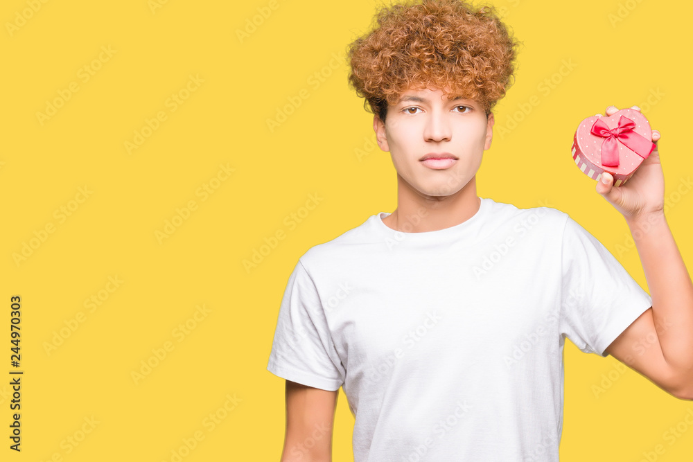 Young handsome man holding heart box as gift of valentine's day with a confident expression on smart face thinking serious Young handsome man holding heart box as gift of valentine's day with a confident expression on smart face thinking serious