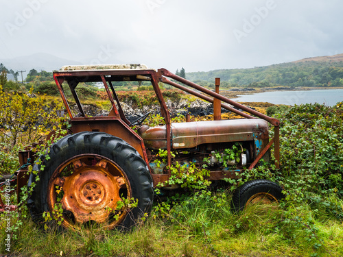 Old rusty tractor overgrown with weeds near a lake photo