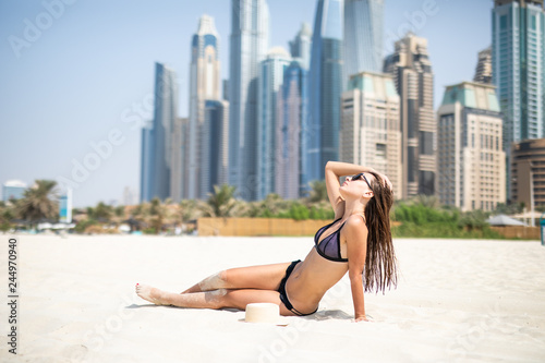 Pretty cheerful woman relaxing at the luxury resort with skyscrapers on background. Girl at Dubai beach. Summer luxury vacation in UAE.