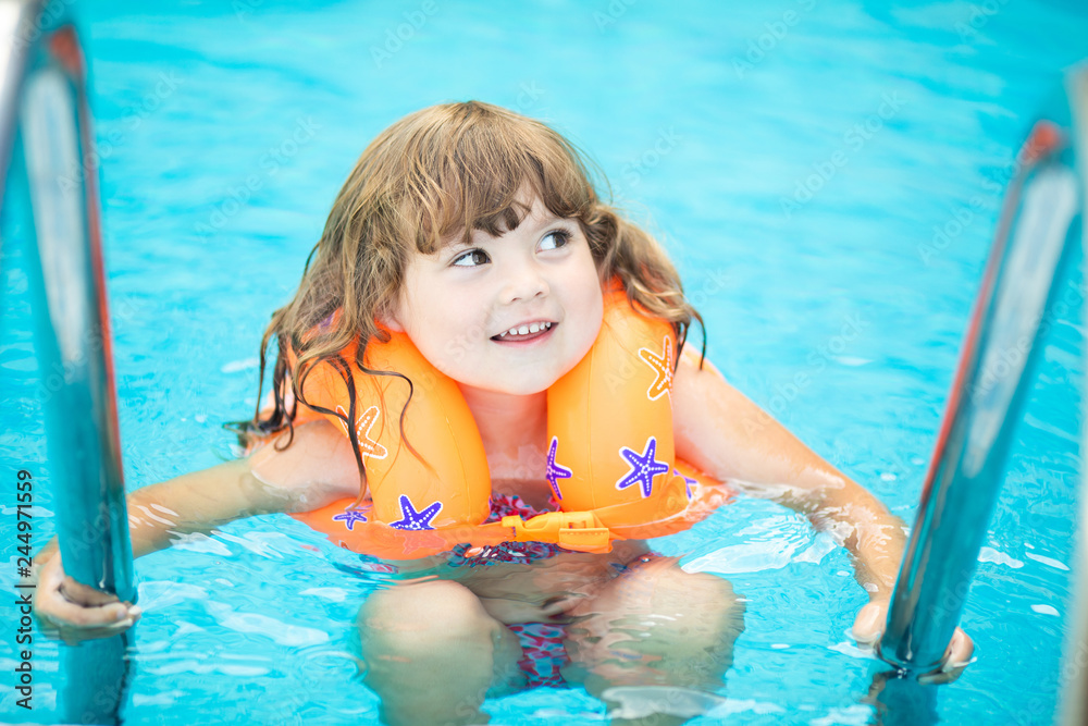 Adorable little girl with inflatable life vest having fun in the pool.