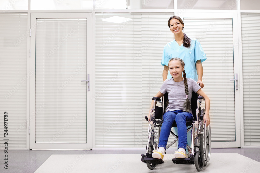 Young female doctor taking care of little girl in wheelchair indoors Young female doctor taking care of little girl in wheelchair indoors