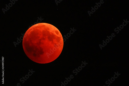 Full red moon over dark black sky background at night. The total phase of the lunar eclipse on July 27, 2018. Moon turning red cause of closer Mars planet to the moon's surface. Copy space.