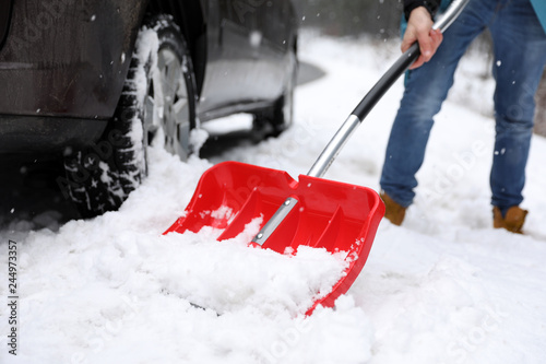 Man cleaning snow with shovel near stuck car outdoors