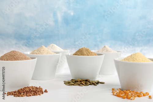 Bowls with different types of flour and seeds on table against color background. Space for text