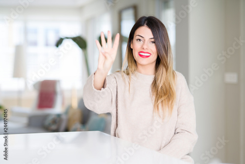 Young beautiful woman wearing winter sweater at home showing and pointing up with fingers number four while smiling confident and happy.