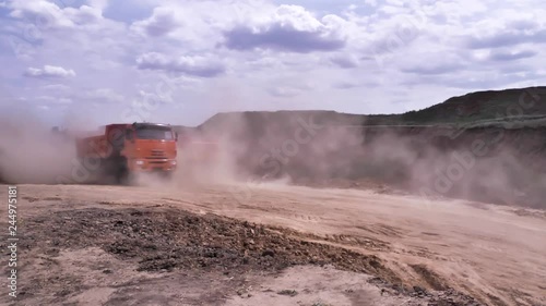 Big, red excavators moving at a sand quarry with flying dust. Scene. Heavy loading dumper trucks on the opencast quarry leaving a thick dust behind. photo